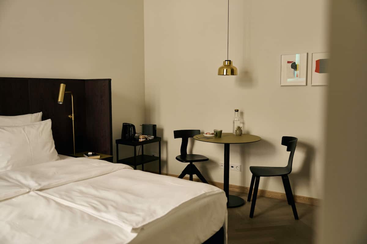 A hotel room with a bed, a desk, two chairs, a table, and a hanging light fixture.
