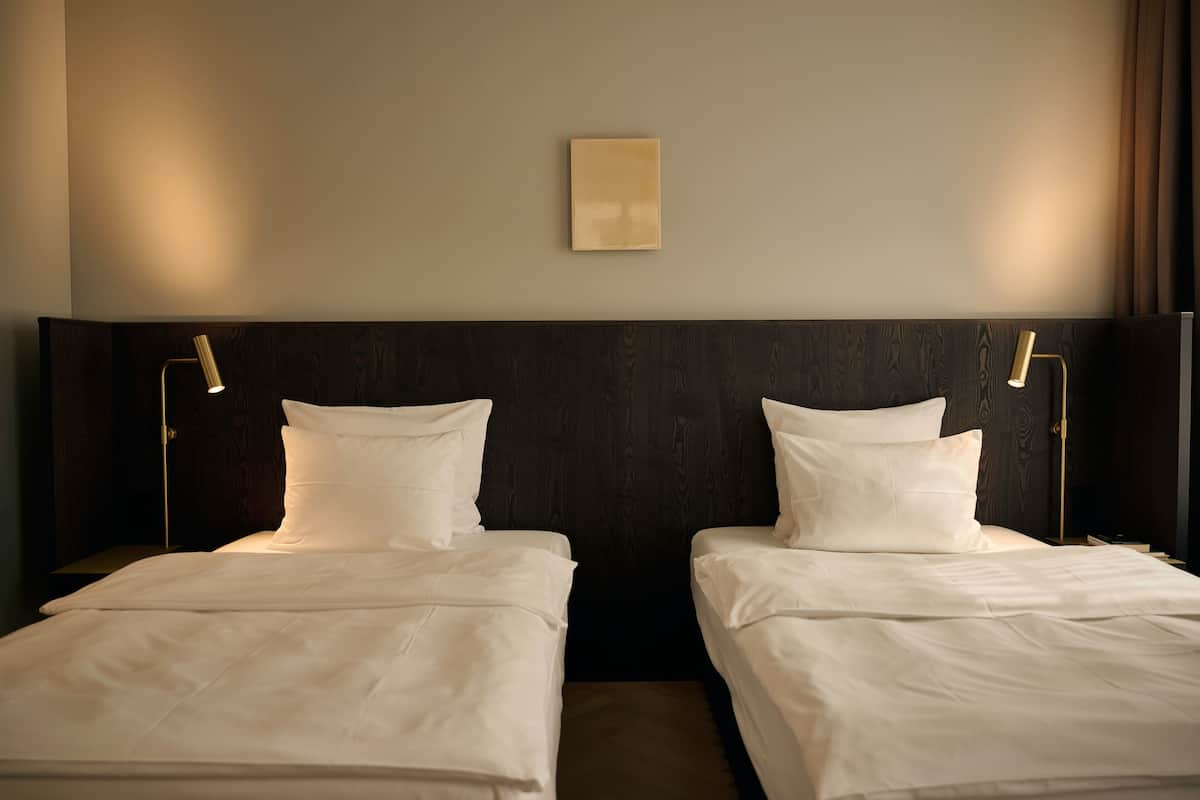 A hotel room with two single beds, a dark wood headboard, and two bedside lamps.
