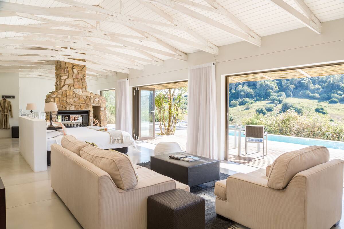 A modern living room with a stone fireplace, a sofa, a coffee table, and a view of a pool and landscape.