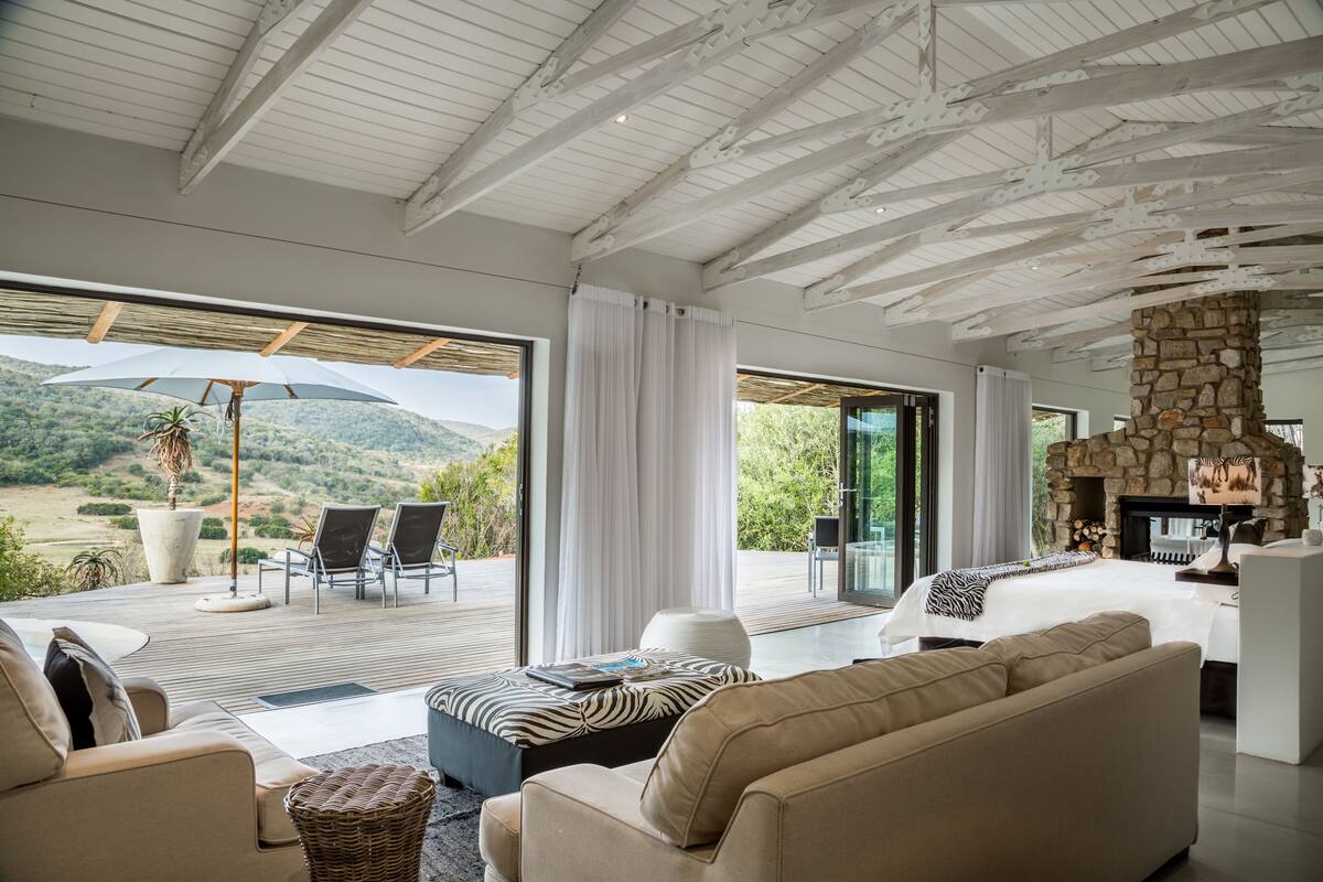 A spacious living area with a large window overlooking a scenic landscape, a stone fireplace, and modern furniture.