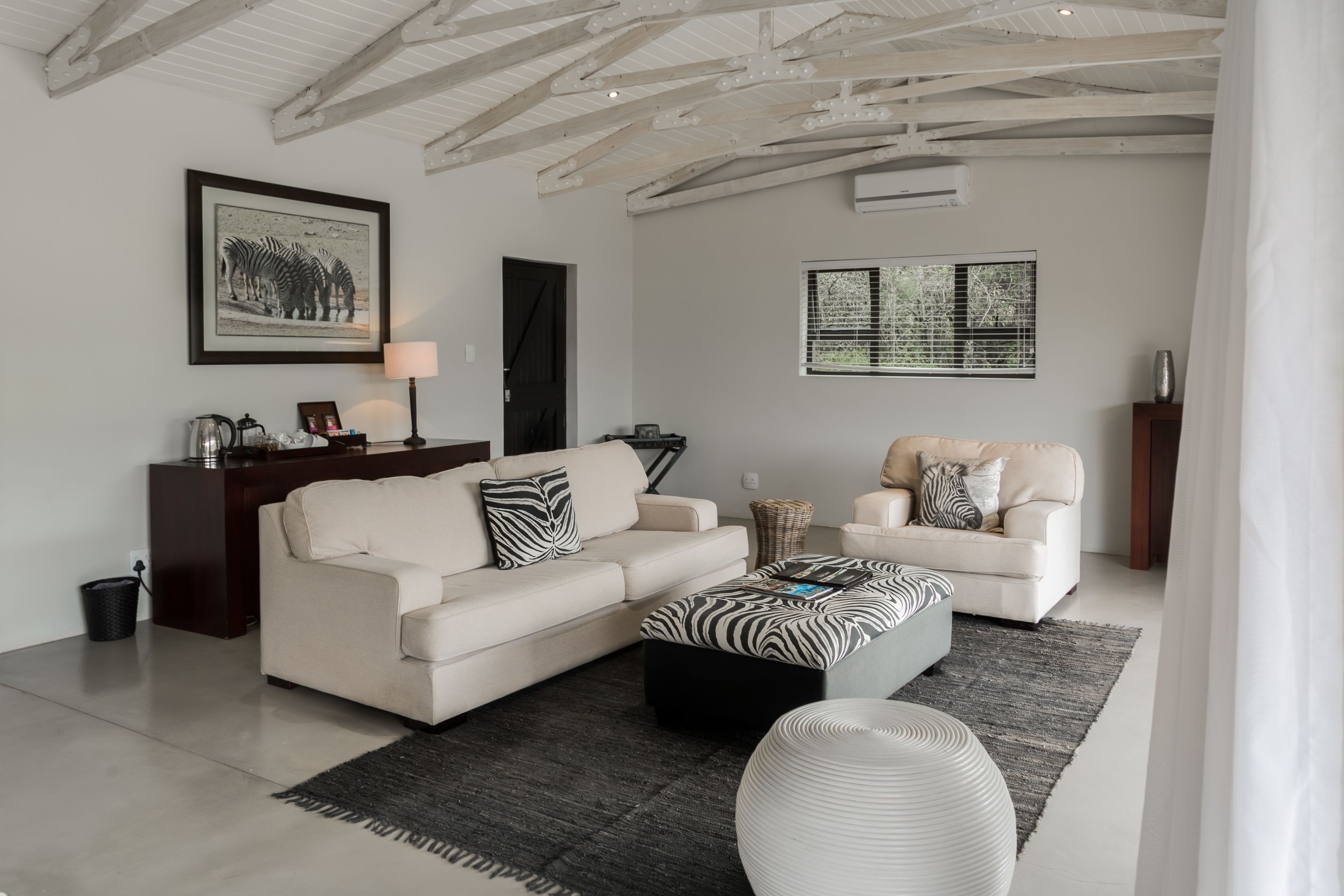 A modern living room with a sofa, a coffee table, and a chair. There is a framed picture on the wall and a window with blinds.