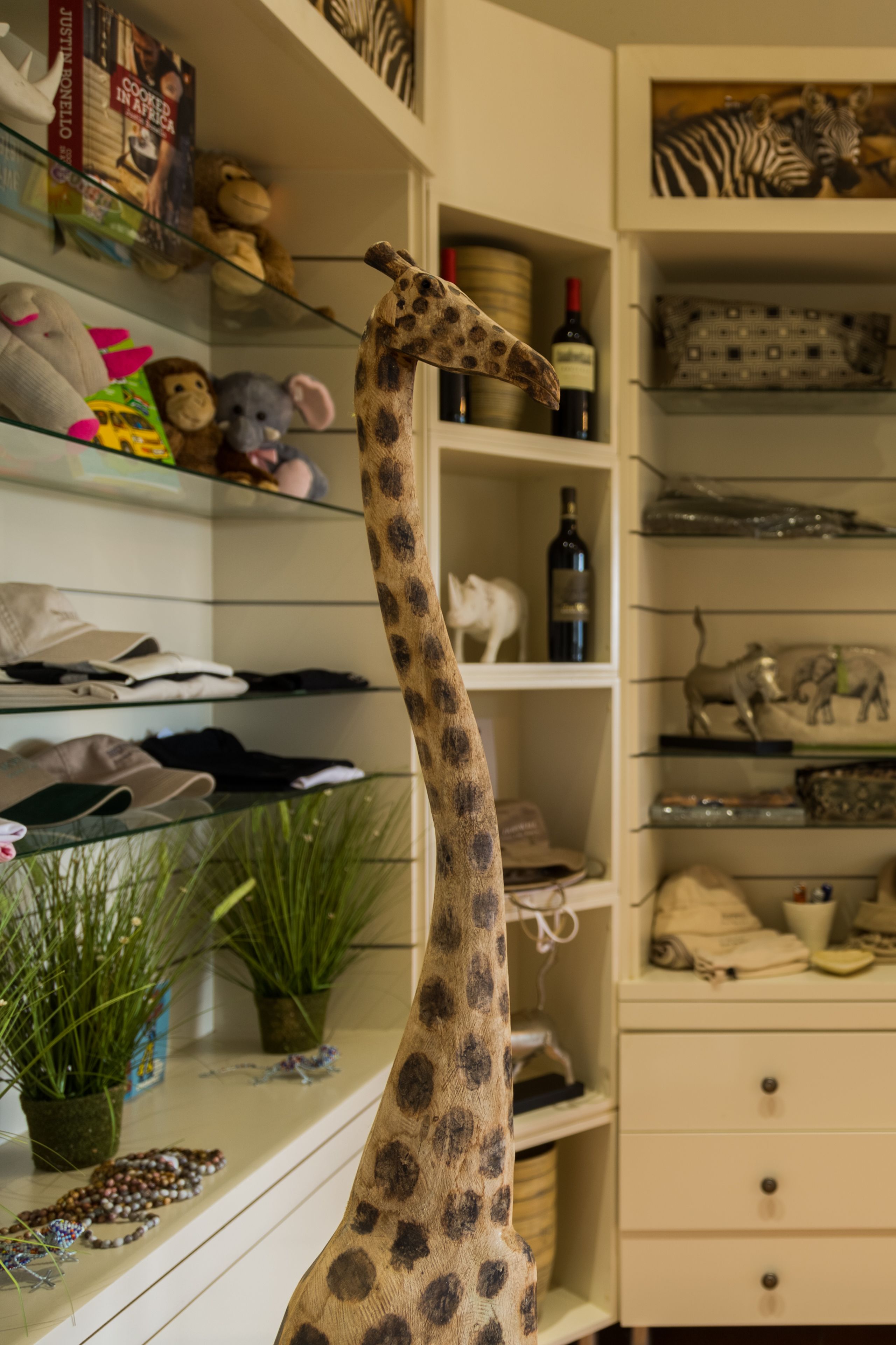 A giraffe figurine in a room with shelves containing books, stuffed animals, and decorative items.