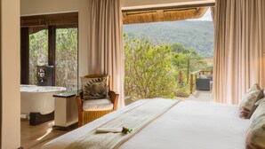 Une chambre dotée d’un grand lit, d’une baignoire et offrant une vue sur un paysage luxuriant.