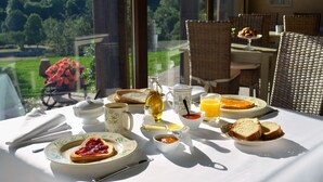Una mesa de desayuno dispuesta con tostadas, mermelada, mantequilla, una jarra de jugo de naranja y una tetera.