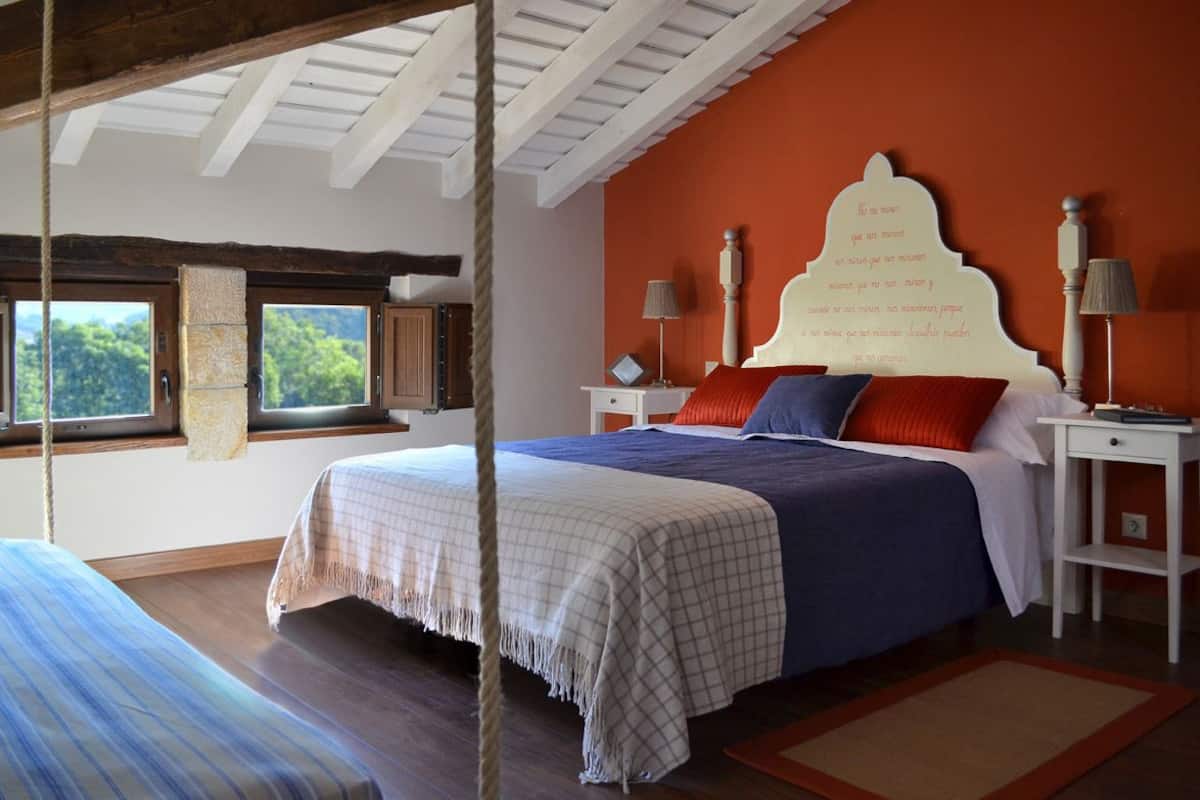 A bedroom with a large bed, two bedside tables, and a window with a view of greenery.