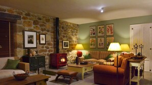 Una sala de estar acogedora con pared de piedra, chimenea, sofá, mesa de centro y lámpara.