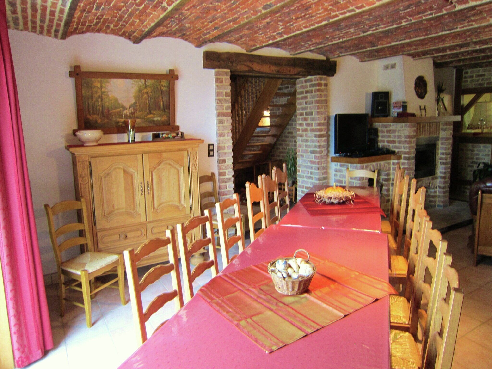 A dining area with a long table, wooden chairs, a red tablecloth, and a basket of bread.