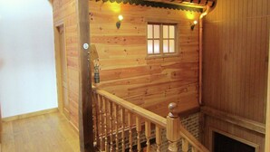 A wooden interior with a wooden staircase, a window with bars, and a lantern on the wall.