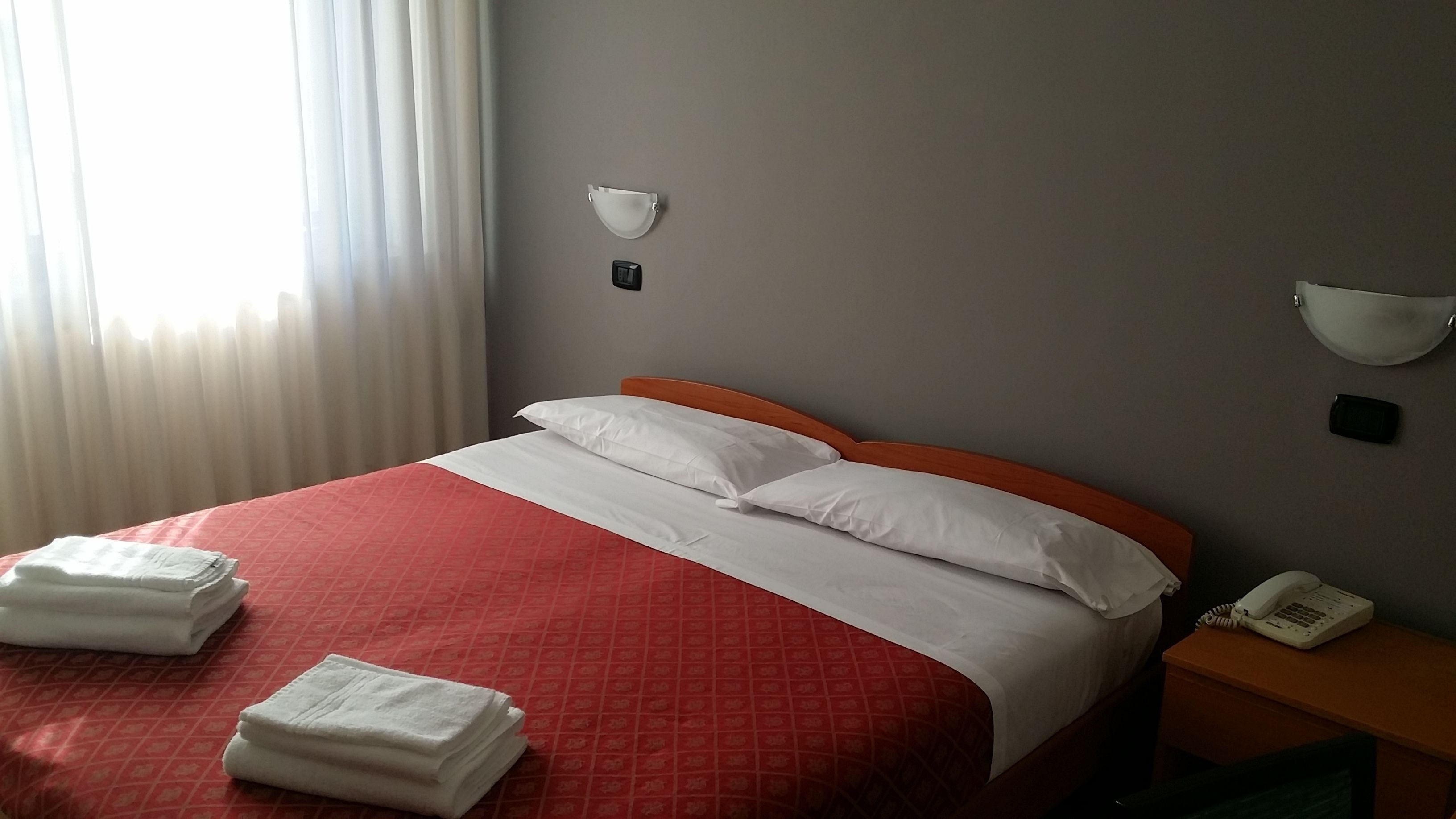 Una habitación de hotel con una cama, dos mesitas de noche, un teléfono y una ventana con cortinas.
