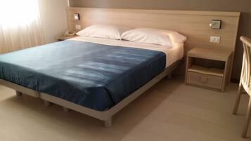 A bed with a blue bedspread, a wooden headboard, a bedside table with a lamp, and a nightstand with a phone.