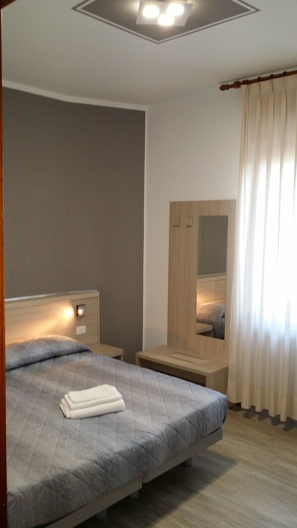 Una habitación de hotel moderna con una cama grande, mesitas de noche, un espejo y una ventana con cortinas.