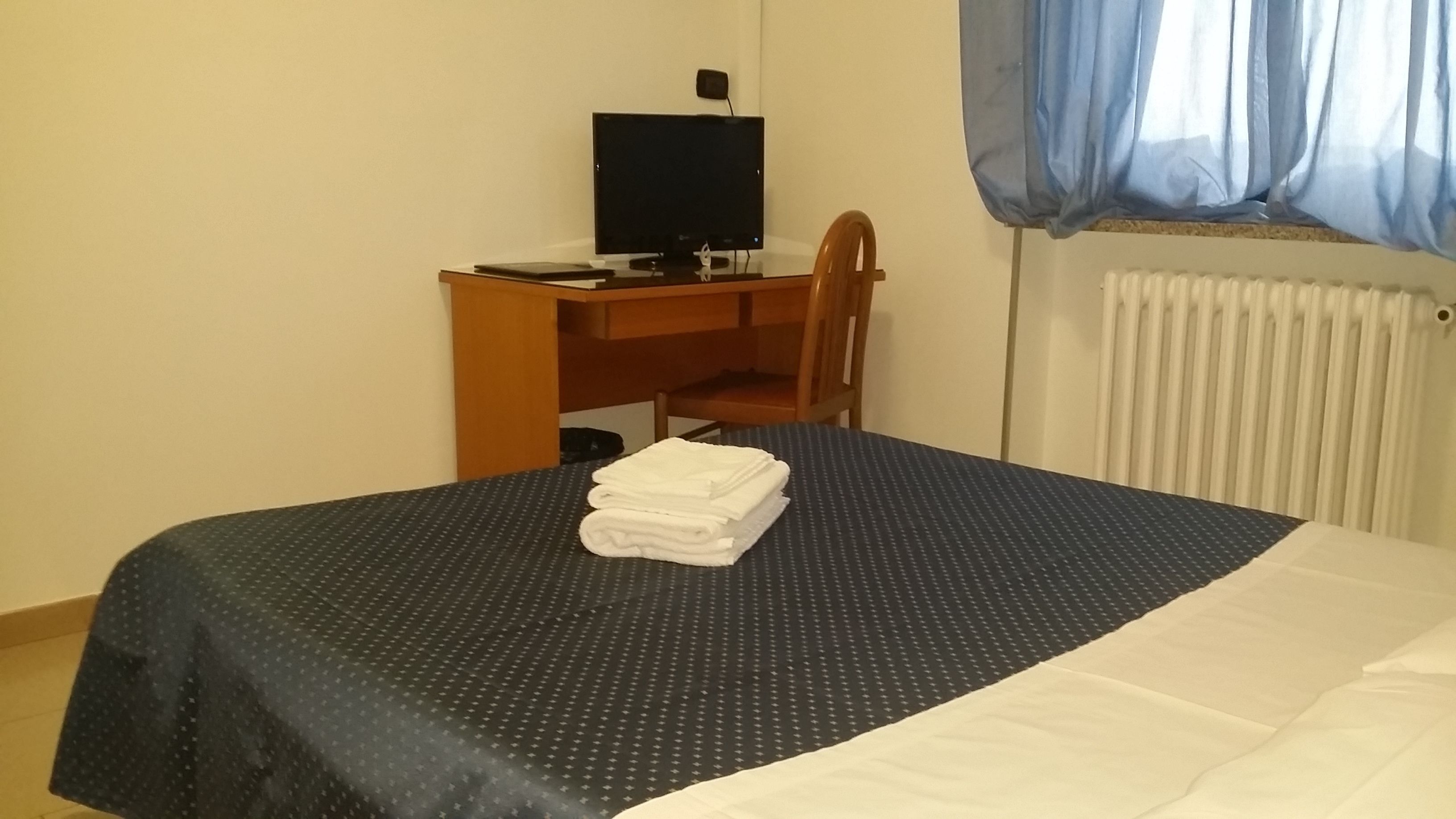 A hotel room with a bed, a desk with a computer and a TV, and a window with curtains.