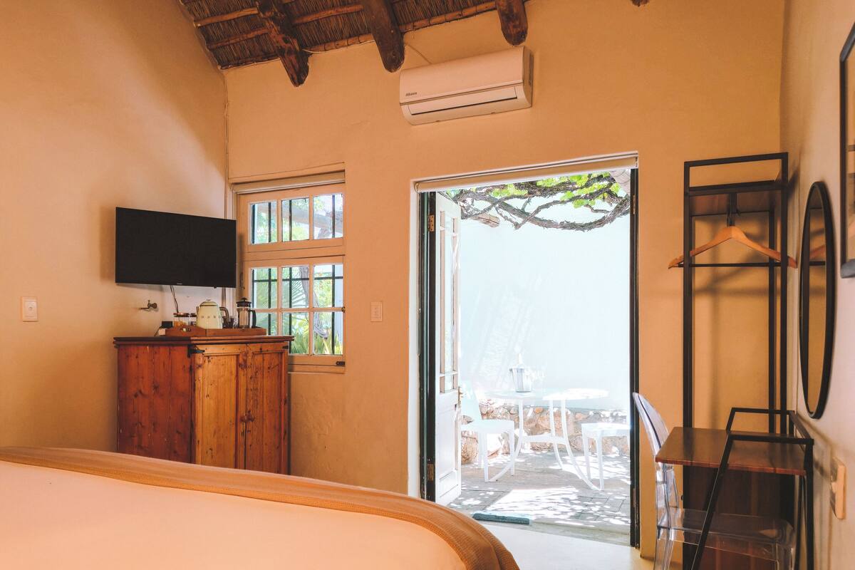 A bedroom with a bed, wooden cabinet, TV, and a view of an outdoor patio with chairs and a table.