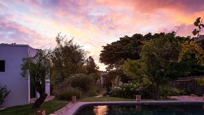 A swimming pool with a clear reflection of the sky and surrounding trees. - Onse Rus Guest House (Prince Albert)