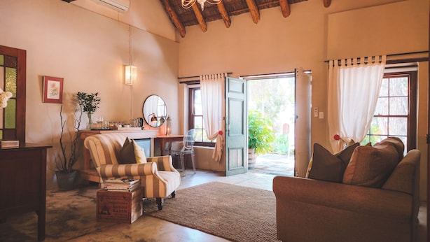A cozy living room with striped armchairs, a coffee table, and a bookshelf. A large mirror hangs on the wall, and a window with curtains is visible. - Onse Rus Guest House (Prince Albert)
