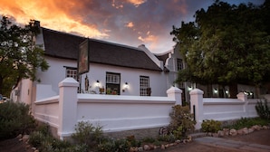 A white building with a thatched roof, a white fence, and a landscaped garden with rocks and plants. - Onse Rus Guest House (Prince Albert)