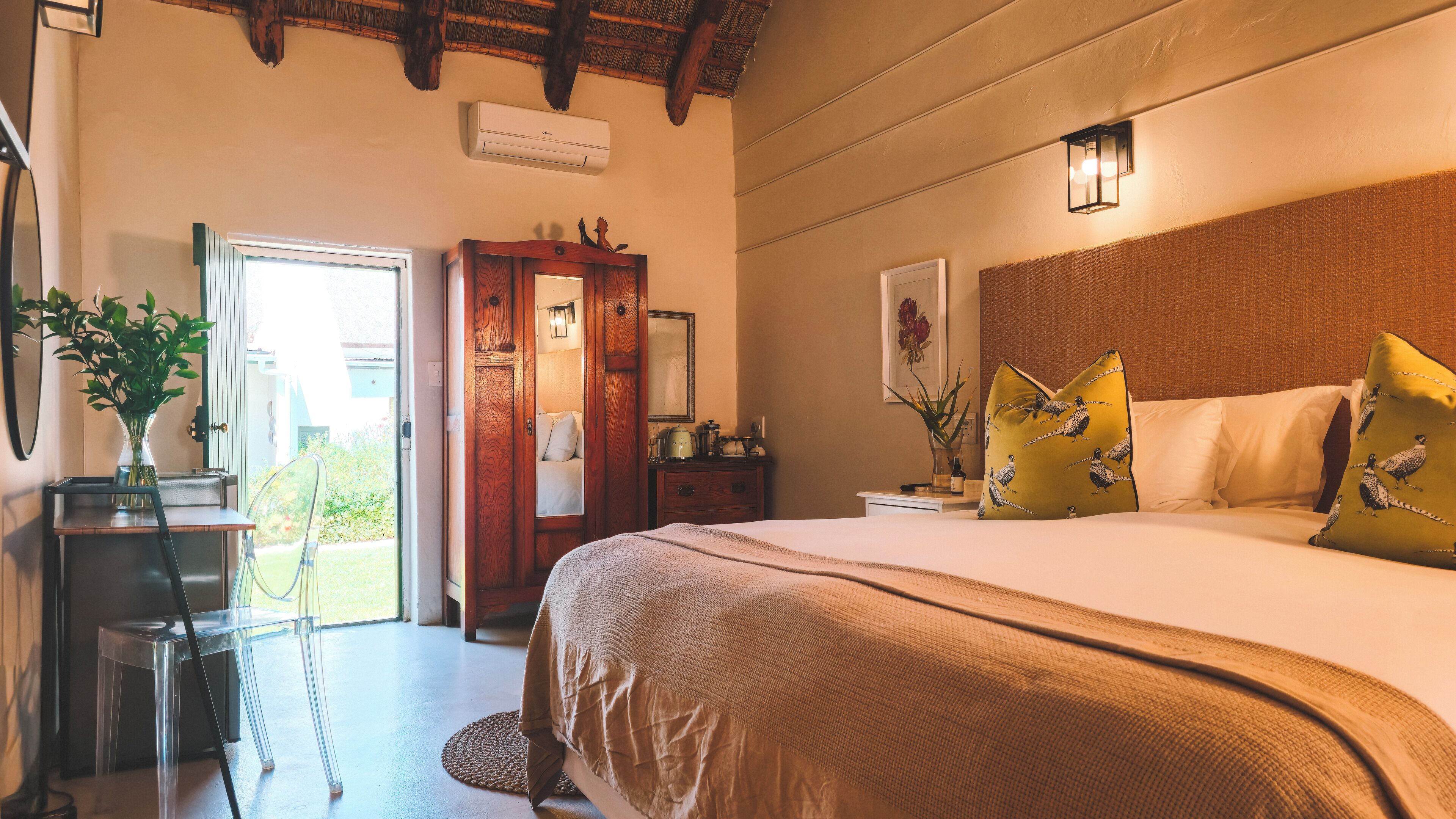 A bedroom with a bed, bedside tables, a mirror, a wooden wardrobe, and a door leading to an outdoor area.