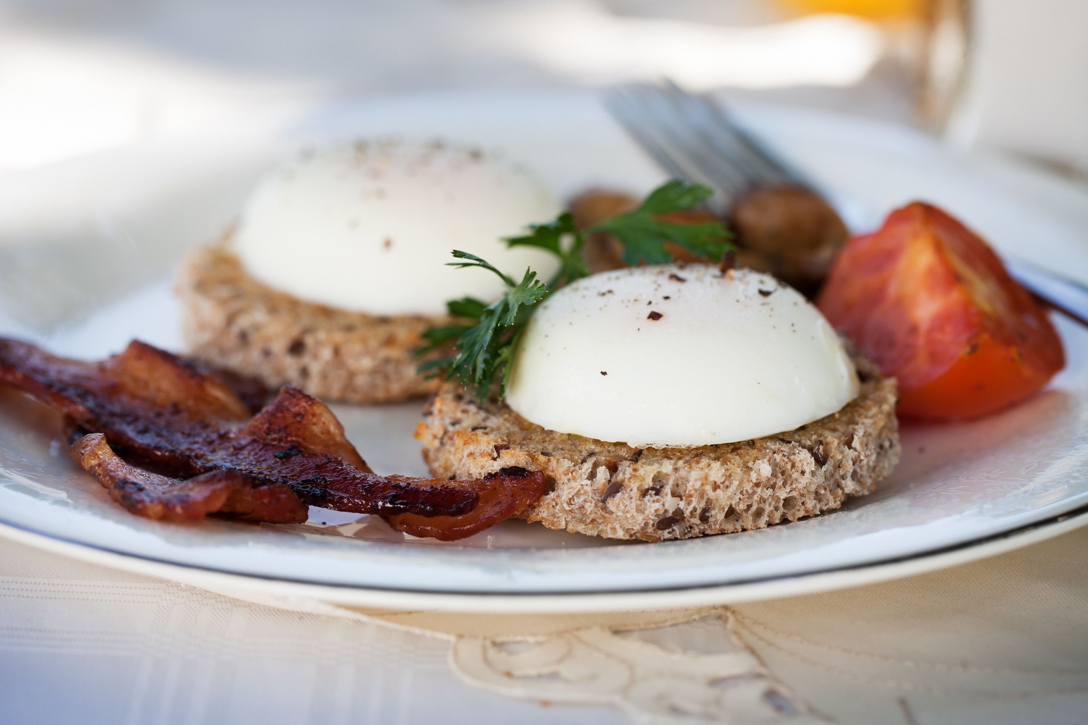 A plate with two open-faced sandwiches topped with poached eggs, bacon, and garnished with parsley.