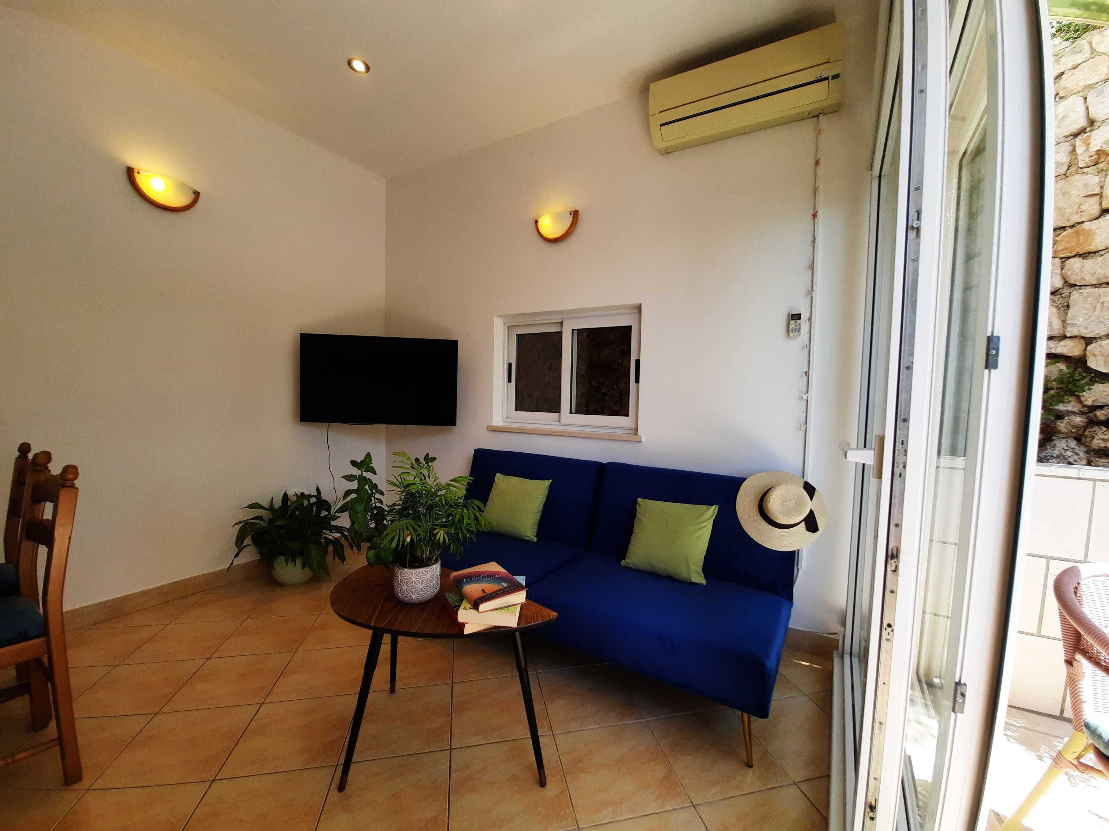 Una sala de estar con un sofá azul, un televisor, una planta en maceta y una mesa de comedor.