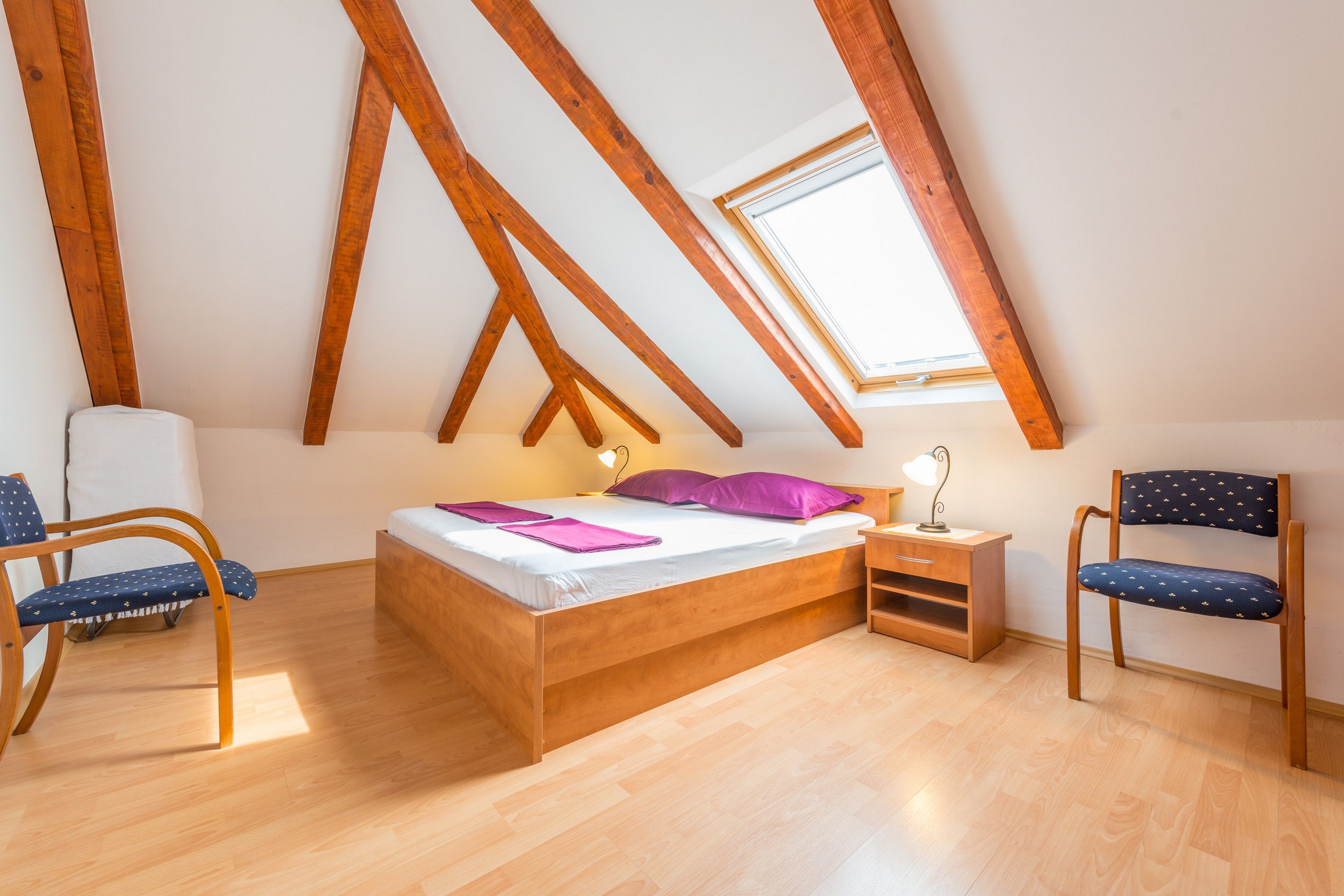 Un dormitorio con una cama de madera, una ventana, una silla y una mesita de noche.