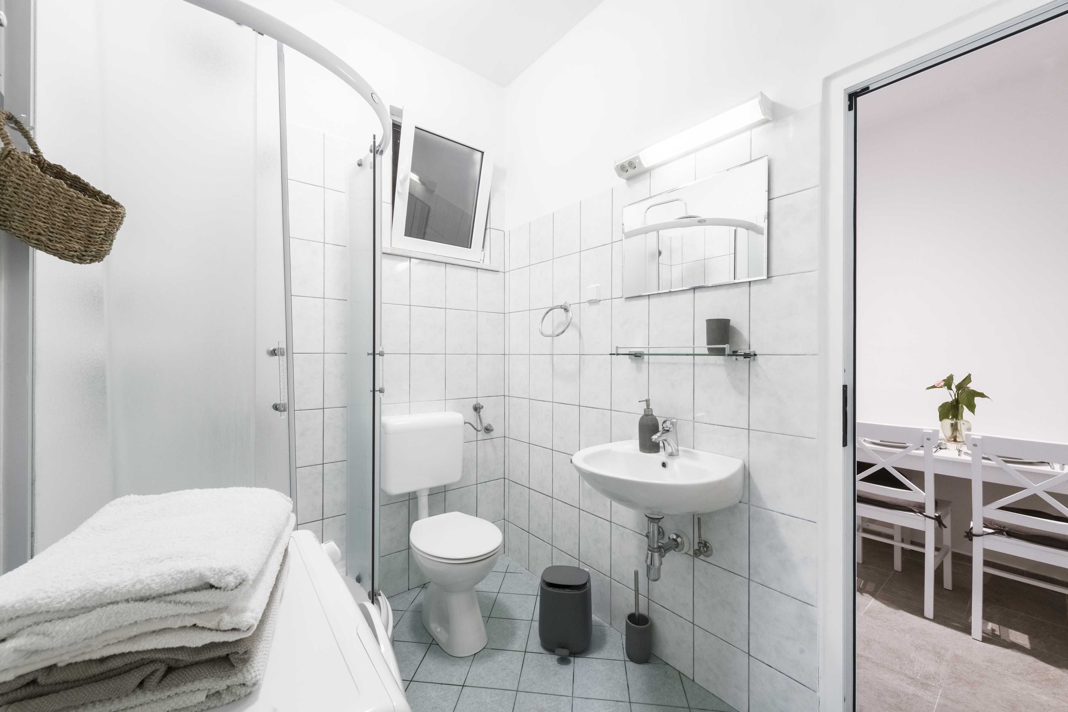 Une salle de bain moderne équipée de toilettes, d’un lavabo et d’une douche. On y trouve également un porte-serviettes et une poubelle.