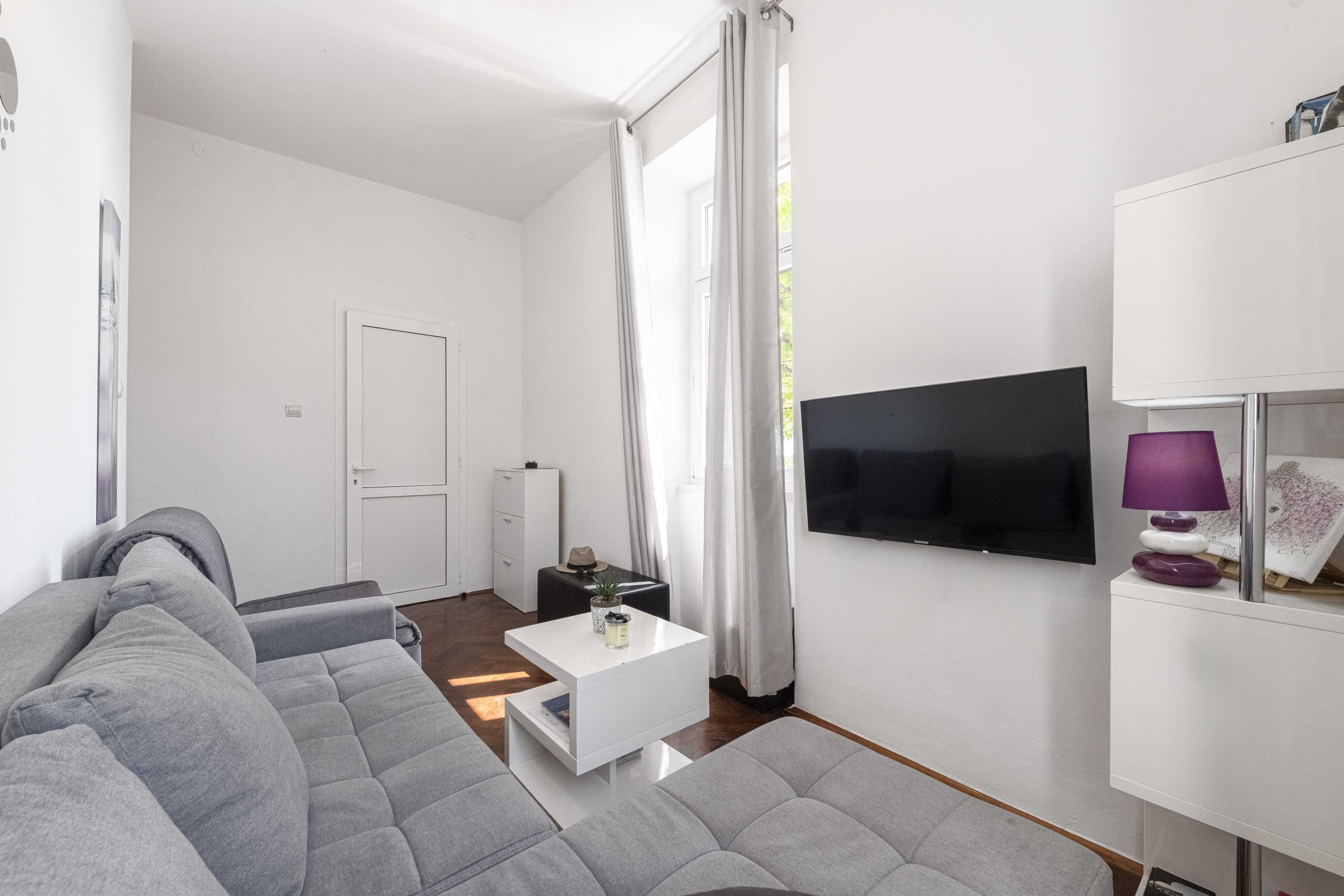 Una sala de estar moderna con un sofá gris, una mesa de centro blanca y un televisor de pantalla plana montado en la pared.