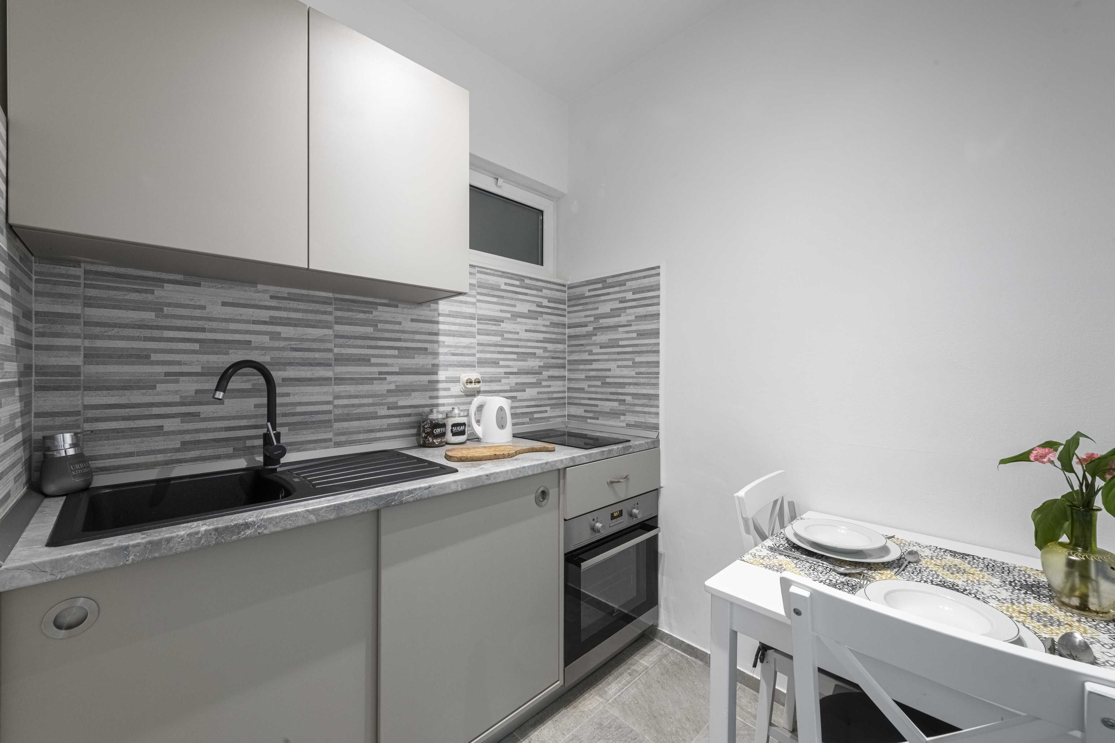 A compact kitchen with a black sink, a microwave, and a small oven. There is a dining table with a white chair and a vase with flowers.