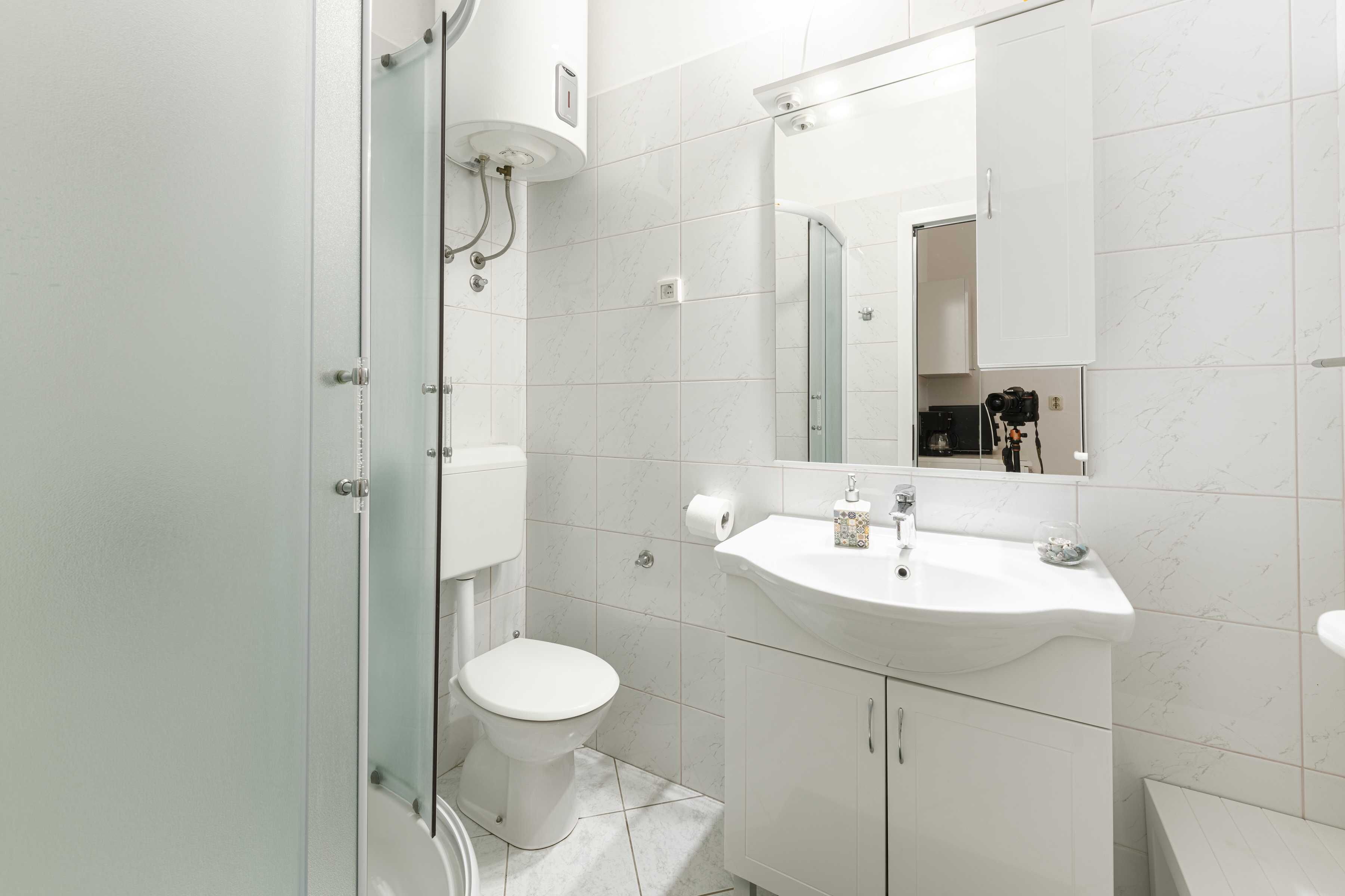 Une salle de bain moderne avec une douche à parois de verre, des toilettes blanches, un lavabo avec un miroir et un meuble de rangement.