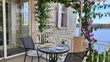 Un balcon avec une table et des chaises, une vue sur la mer et un mur en pierre.