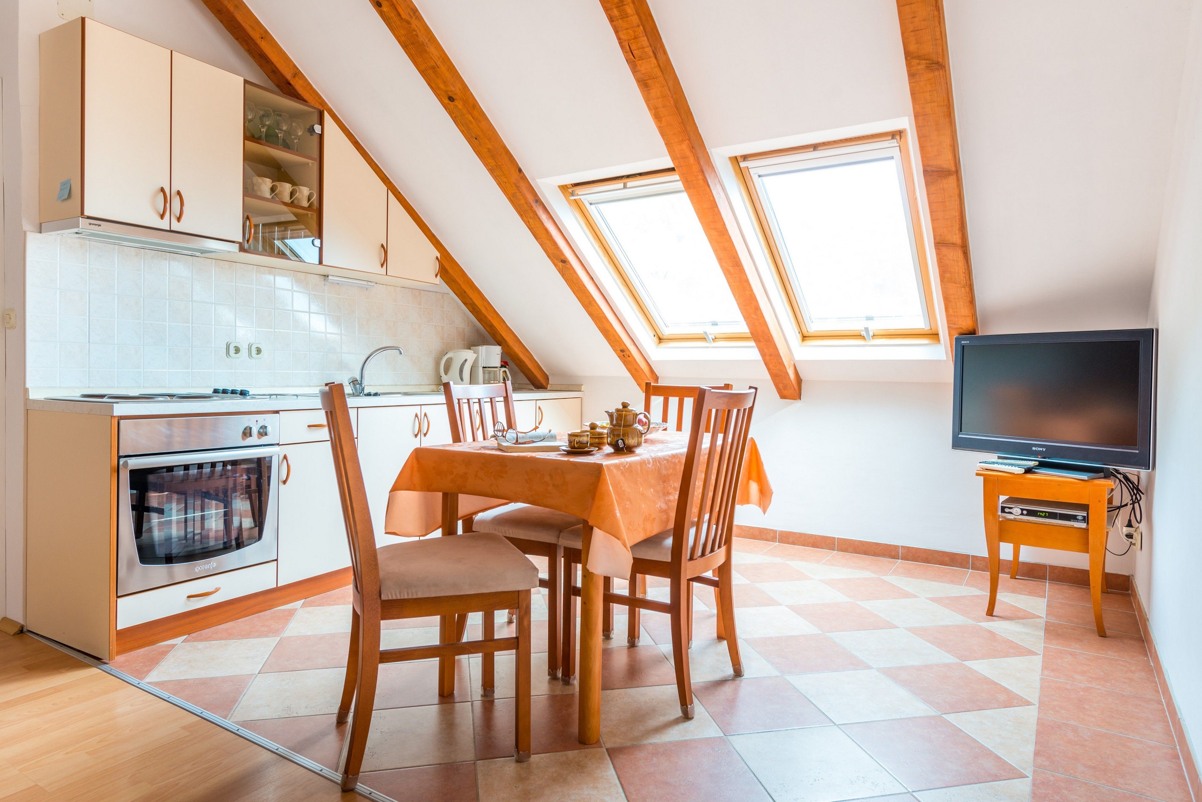 A kitchen with a dining table, chairs, a television, and a window.