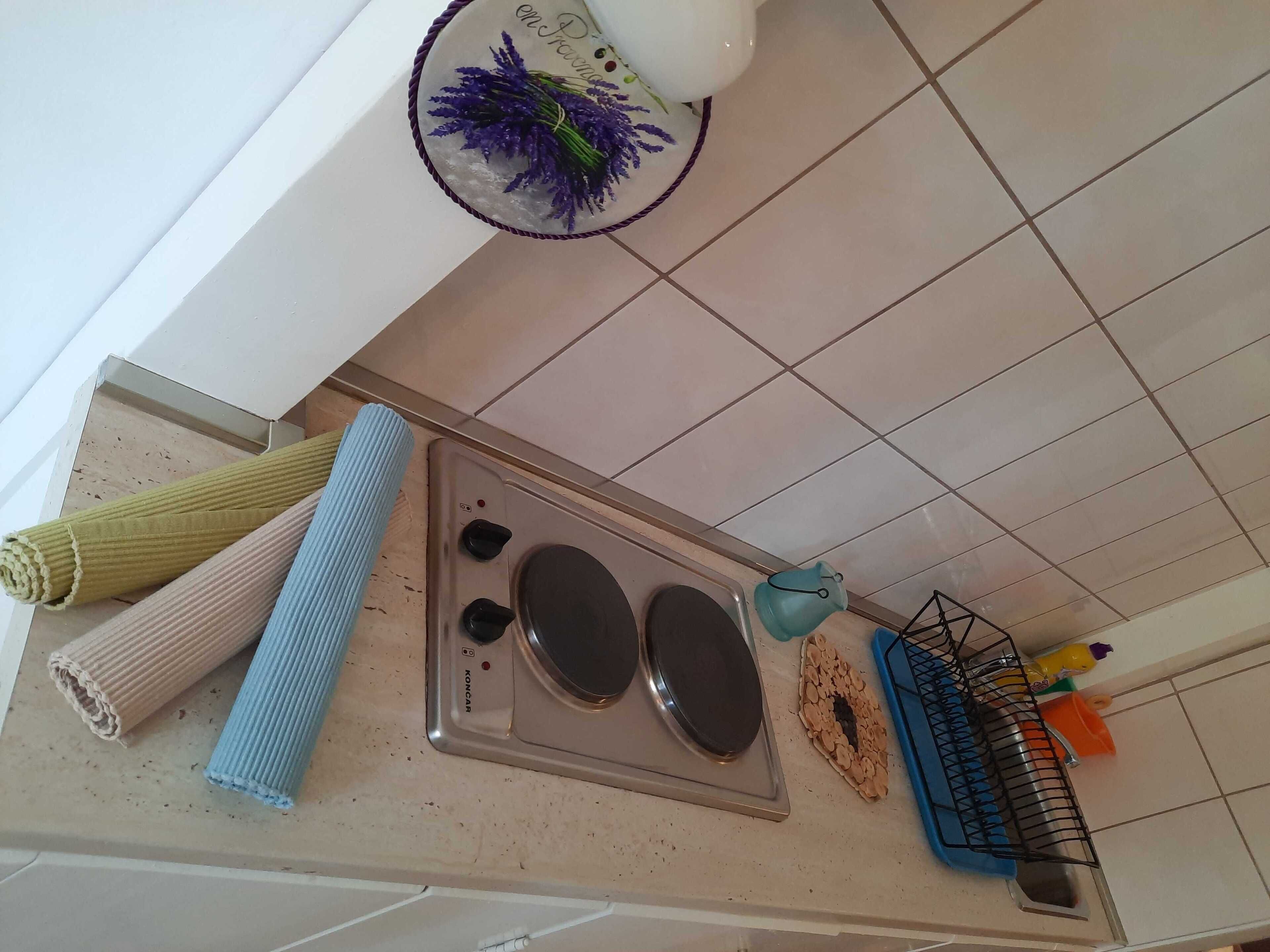 Una cocina con estufa, un hervidor azul y un escurreplatos.