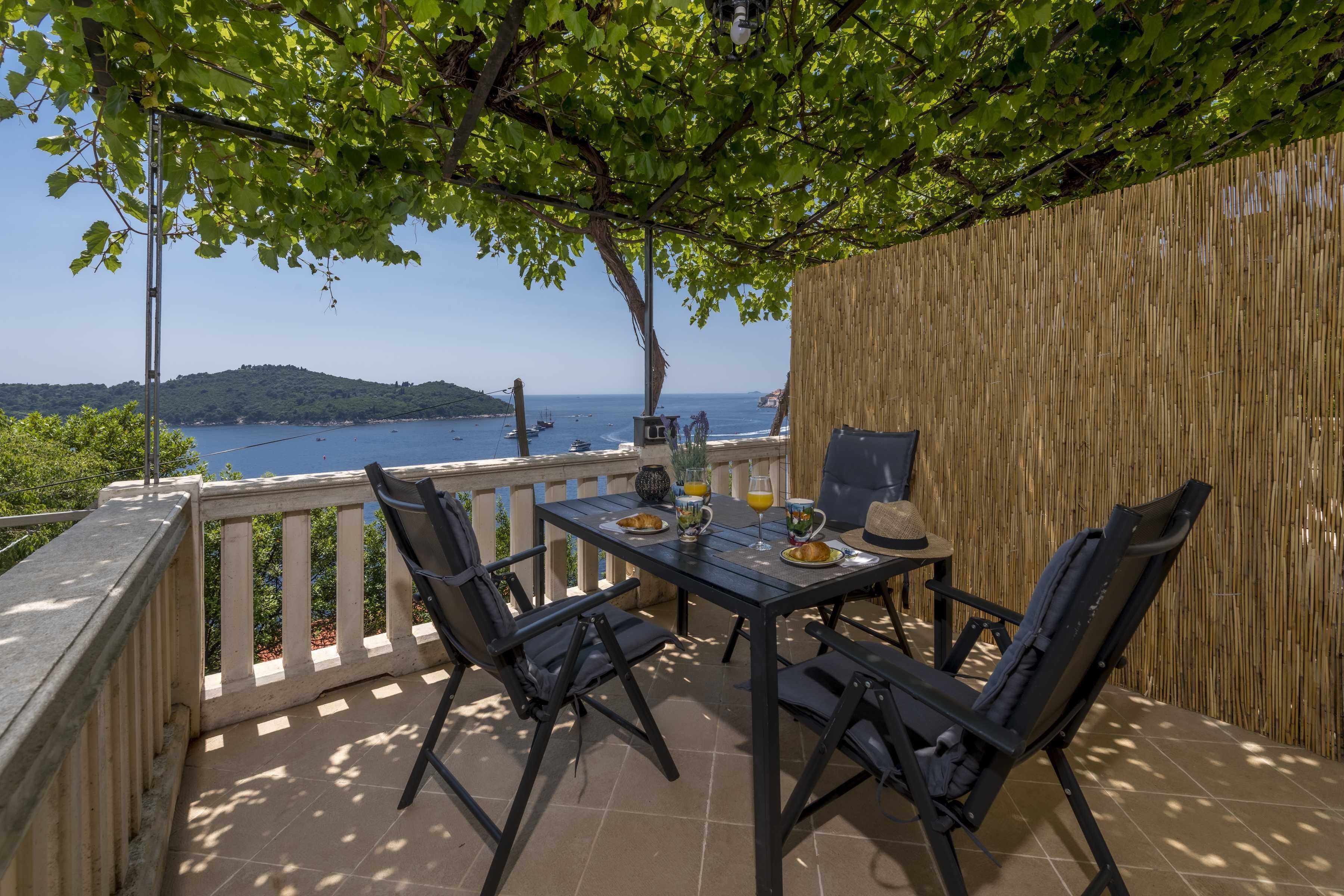 A terrace with a table set for two, overlooking a body of water and a distant hill.