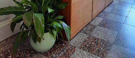 A wooden dresser with a plant beside it, a framed picture on the wall, and a tiled floor.