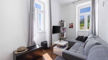 Un salon moderne avec un canapé gris, un pouf noir, une table basse blanche et un téléviseur fixé au mur.