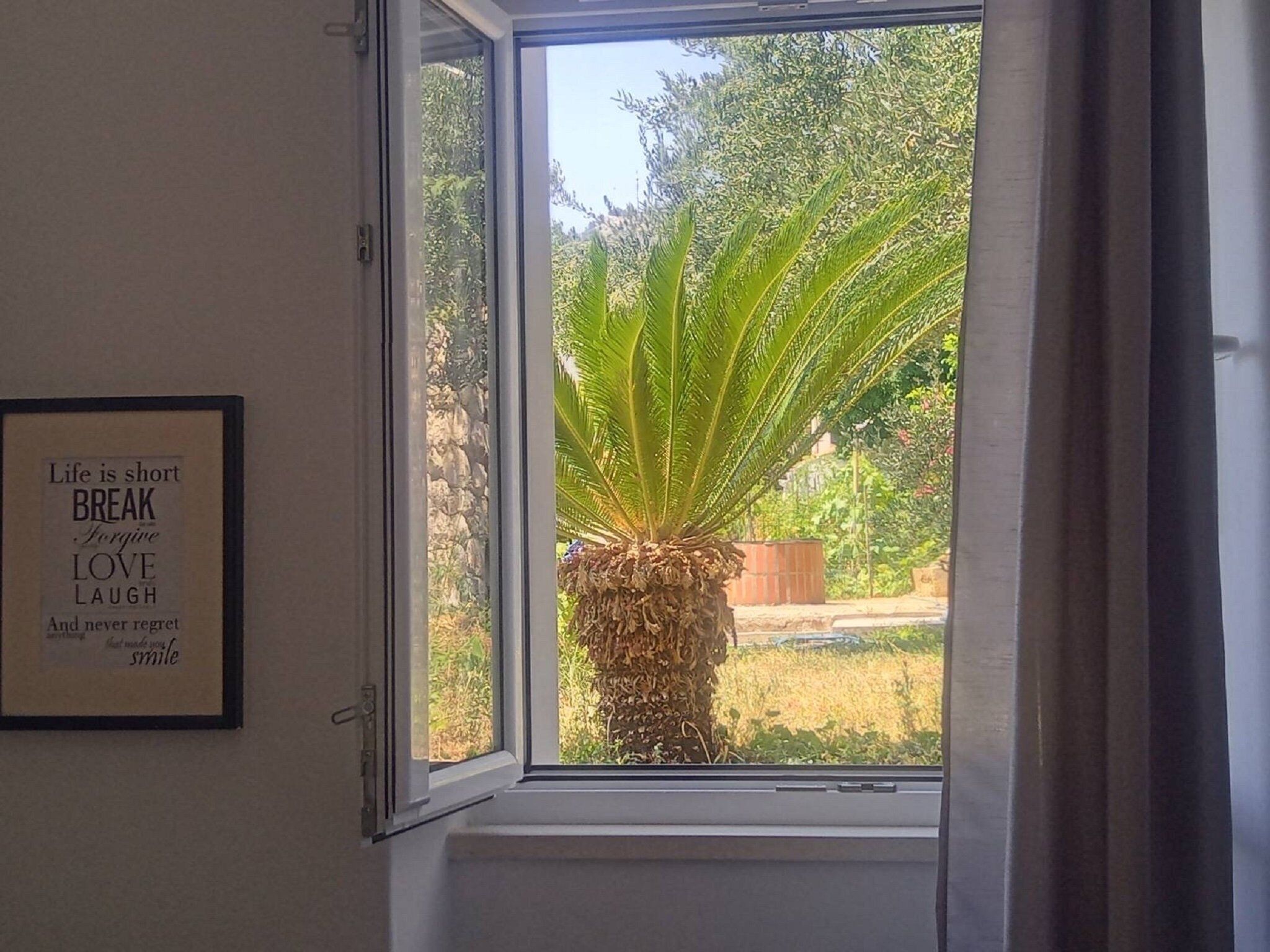 A window with a framed inspirational quote on the wall, a potted plant, and a view of greenery outside.