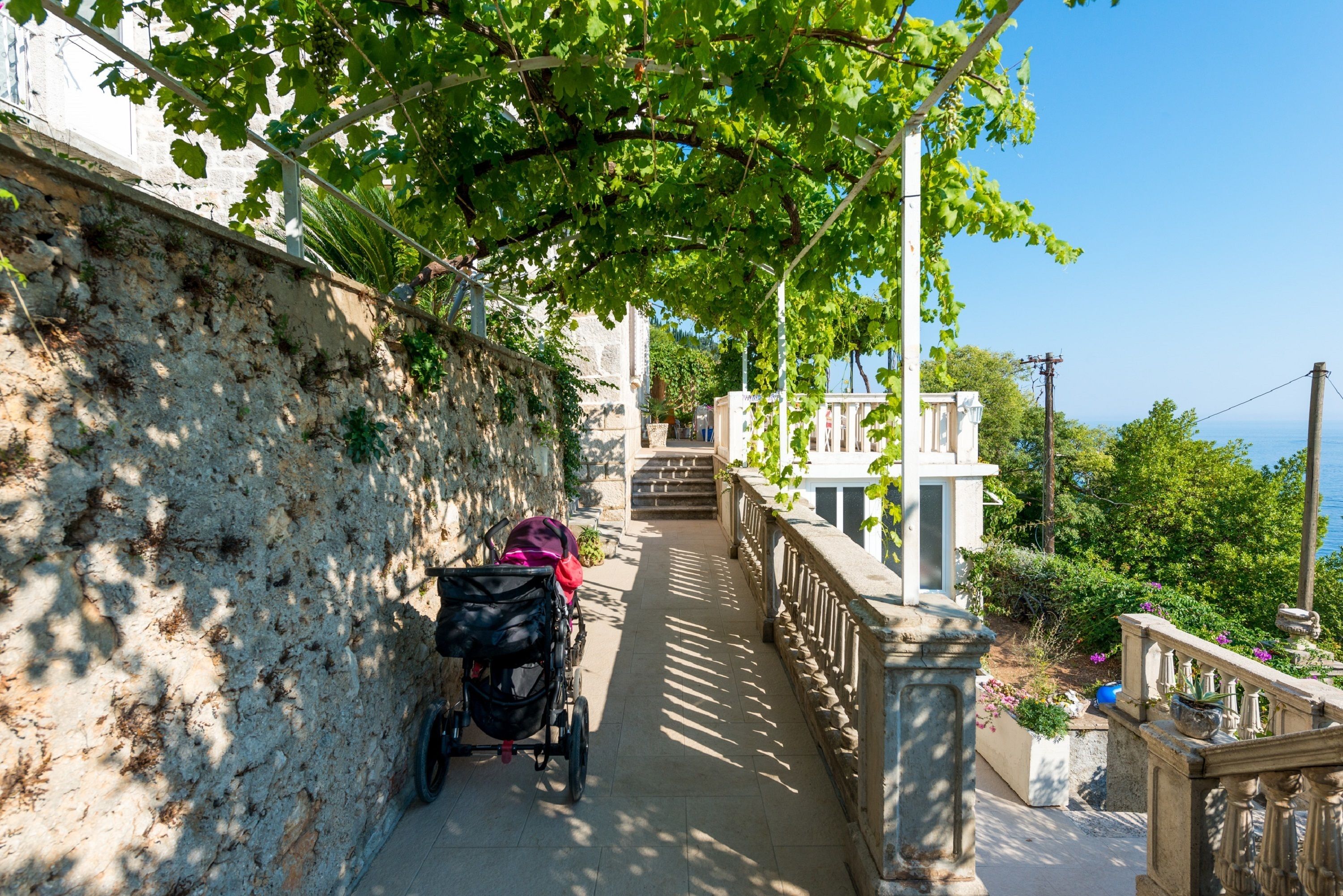 A stone pathway with a stroller, leading to a building with a balcony overlooking a body of water.