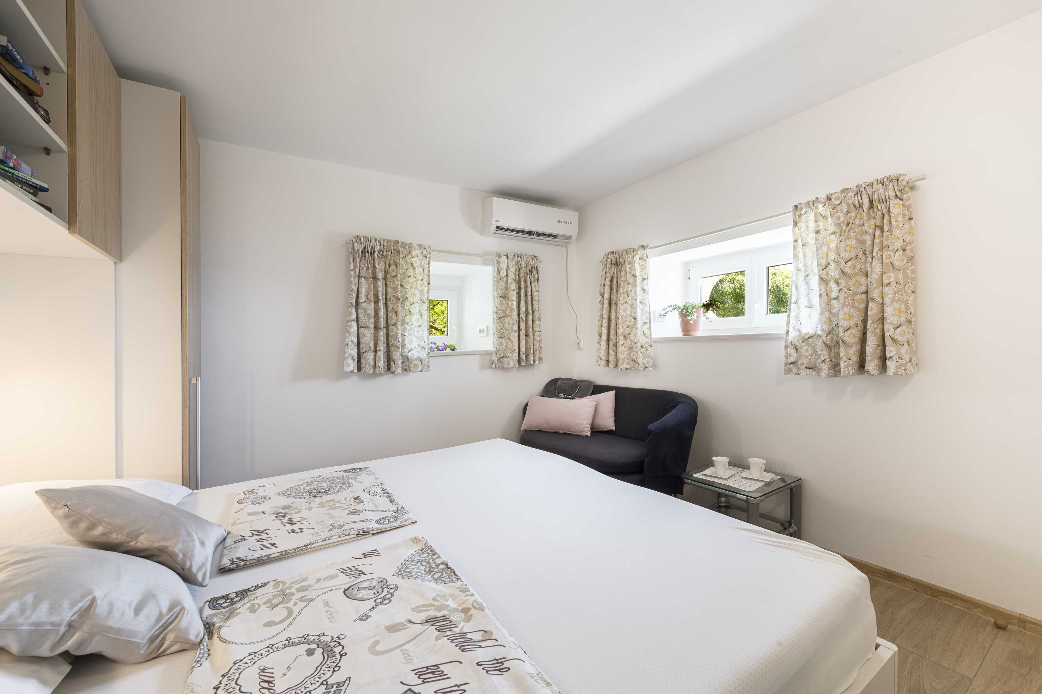 A bedroom with a bed, a desk, a chair, and an air conditioning unit.