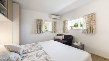 A bedroom with a bed, a desk, a chair, and an air conditioning unit.