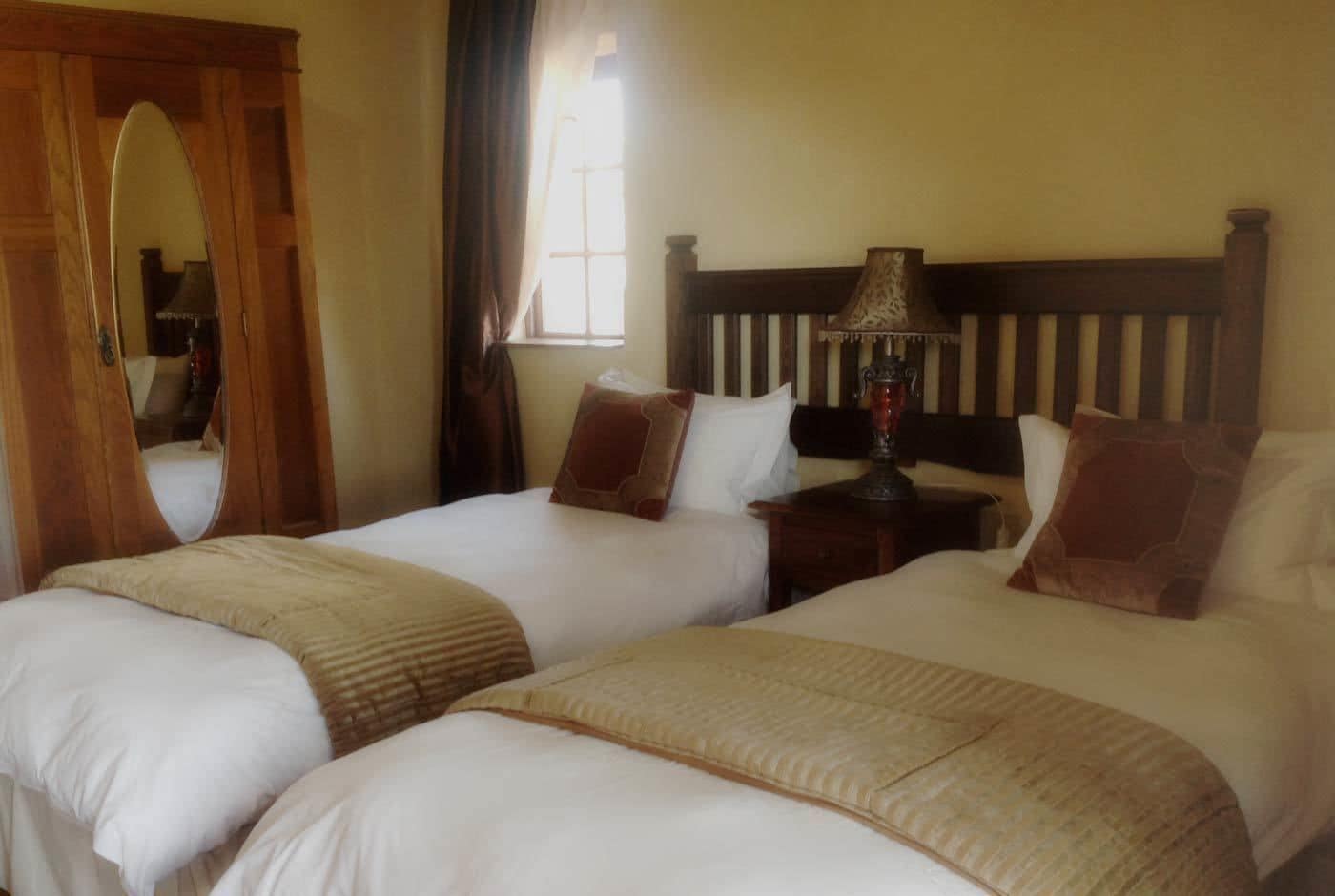 Een hotelkamer met twee bedden, een houten hoofdbord, een nachtkastje met een lamp en een spiegel.