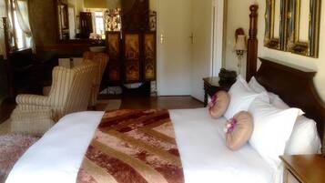 A bedroom with a large bed, a chair, a mirror, and a dresser.