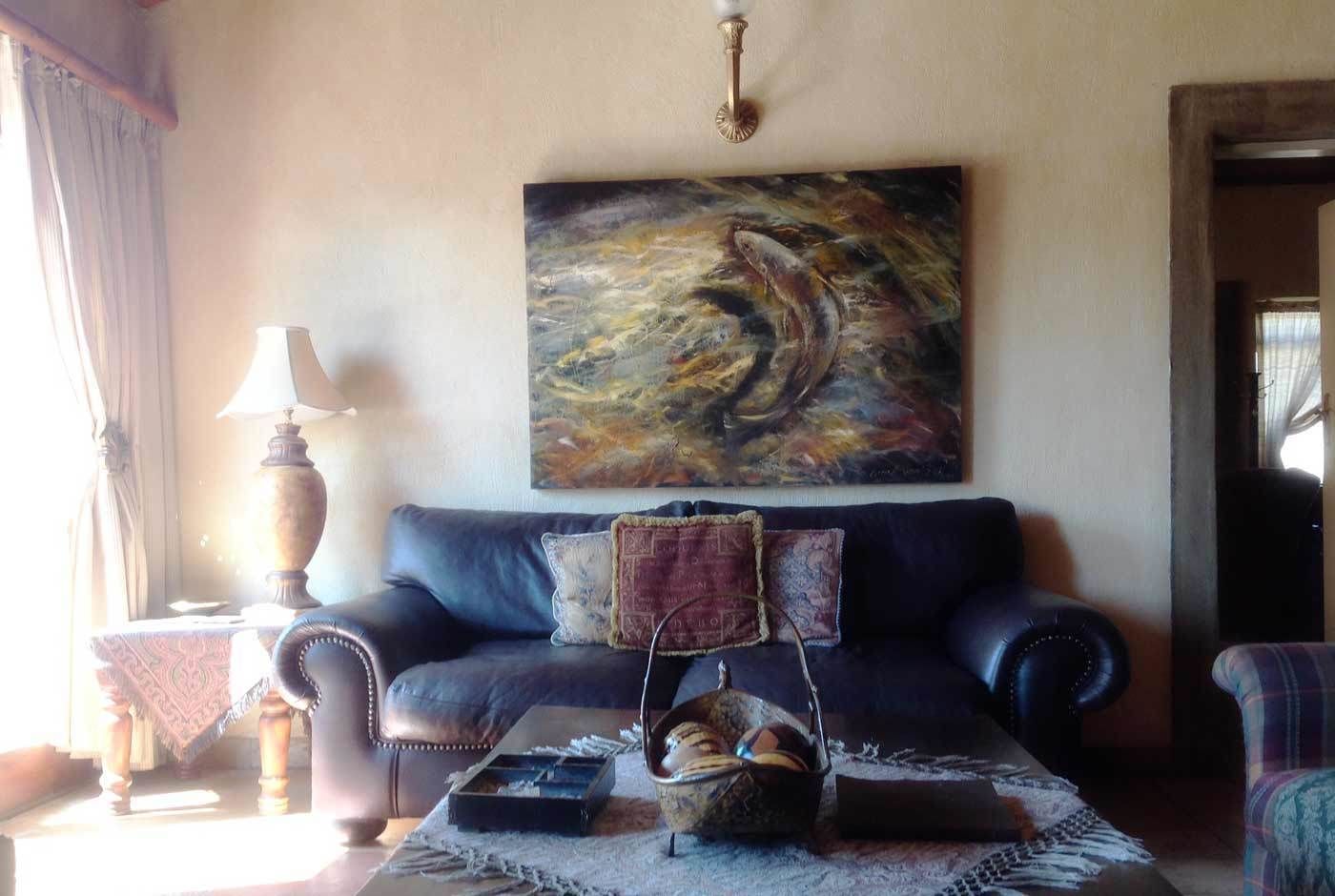 A living room with a dark leather sofa, a painting above it, and a lamp on a side table.