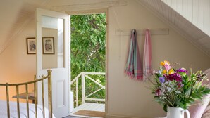 Een slaapkamer met een bed, een witte deur die uitkomt op een balkon, een witte vaas met bloemen en een aan de muur bevestigd handdoekenrek.