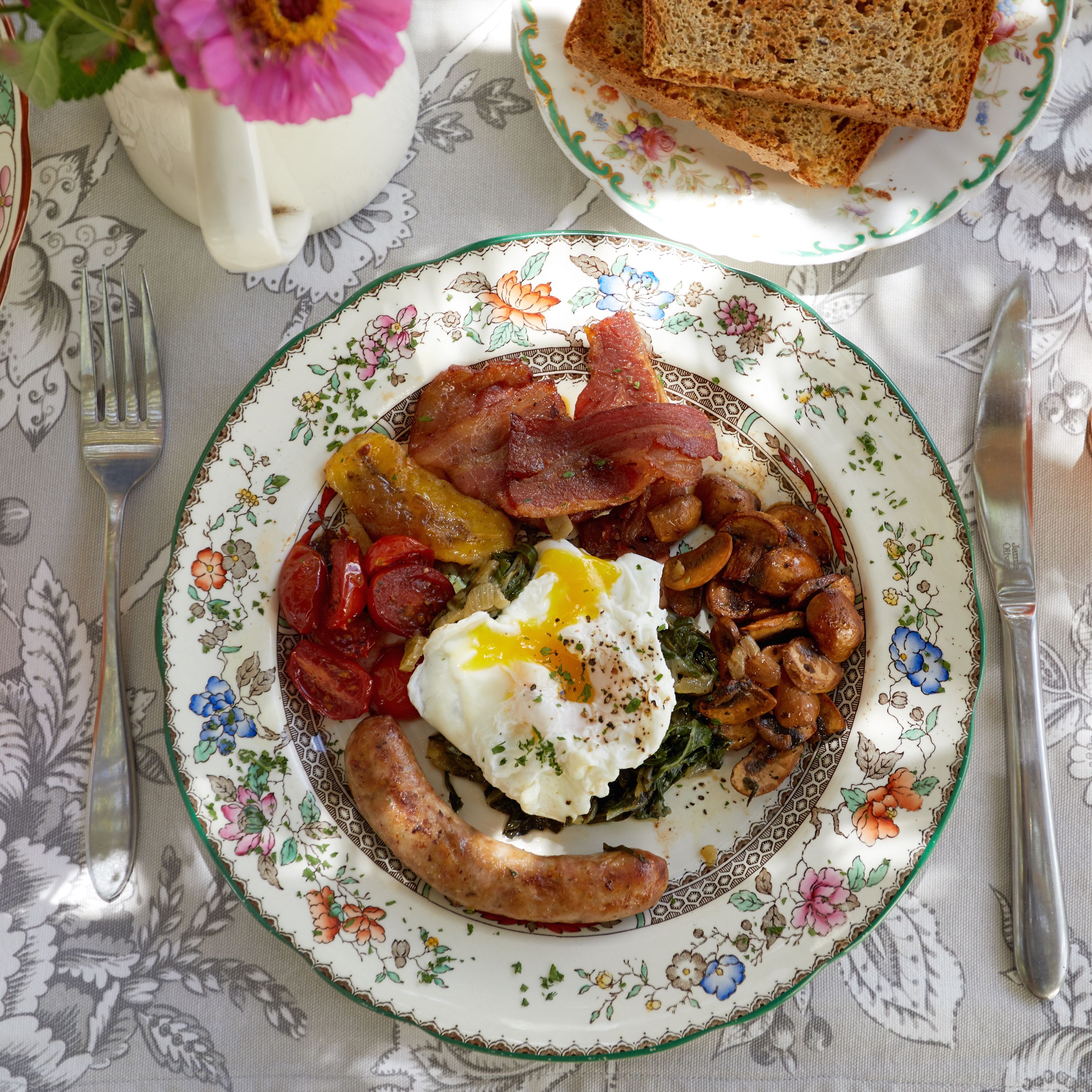 A plate of breakfast food including bacon, sausages, eggs, and mushrooms.