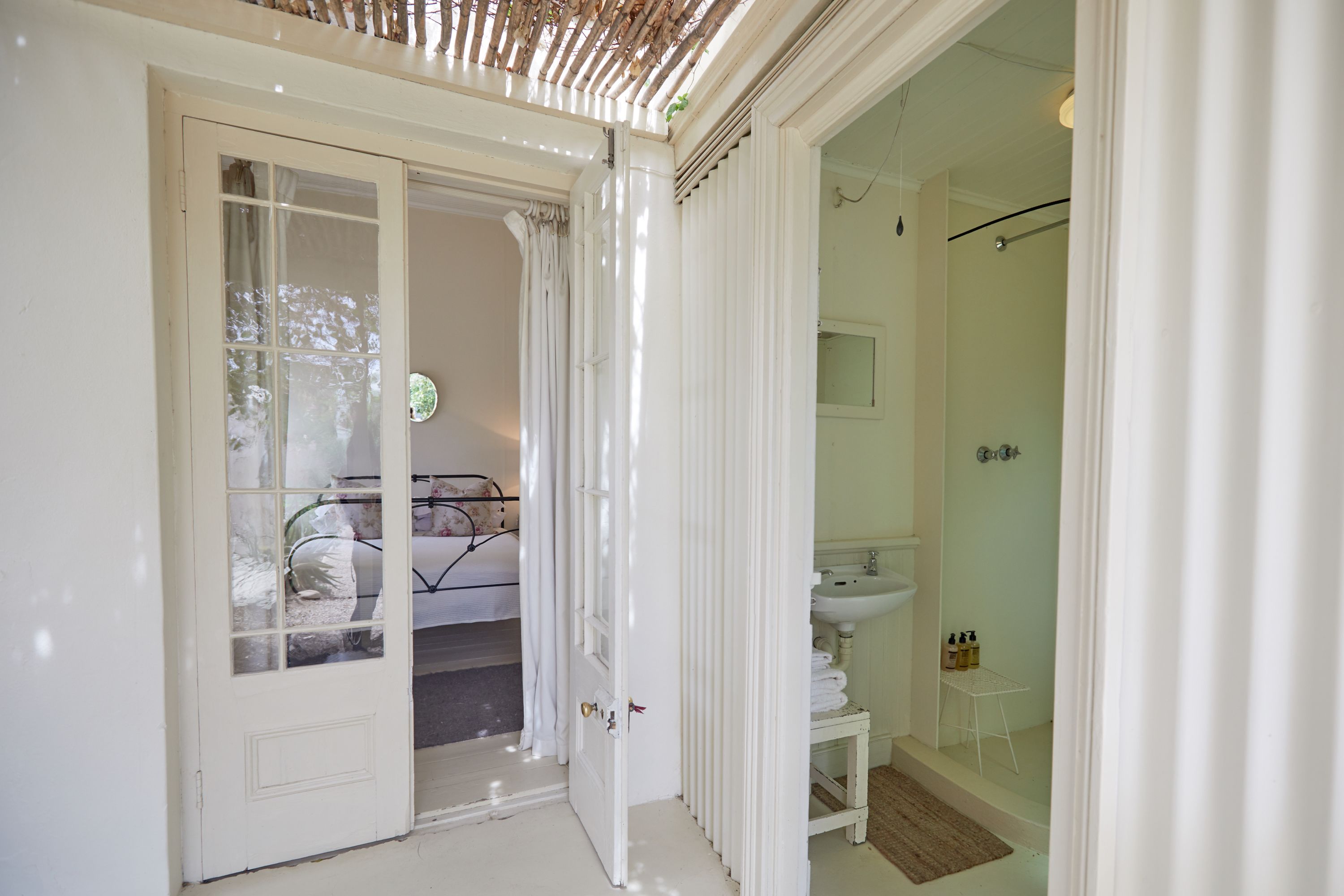 A bedroom with a bed, a bathroom with a sink and shower, and a door leading to another room.