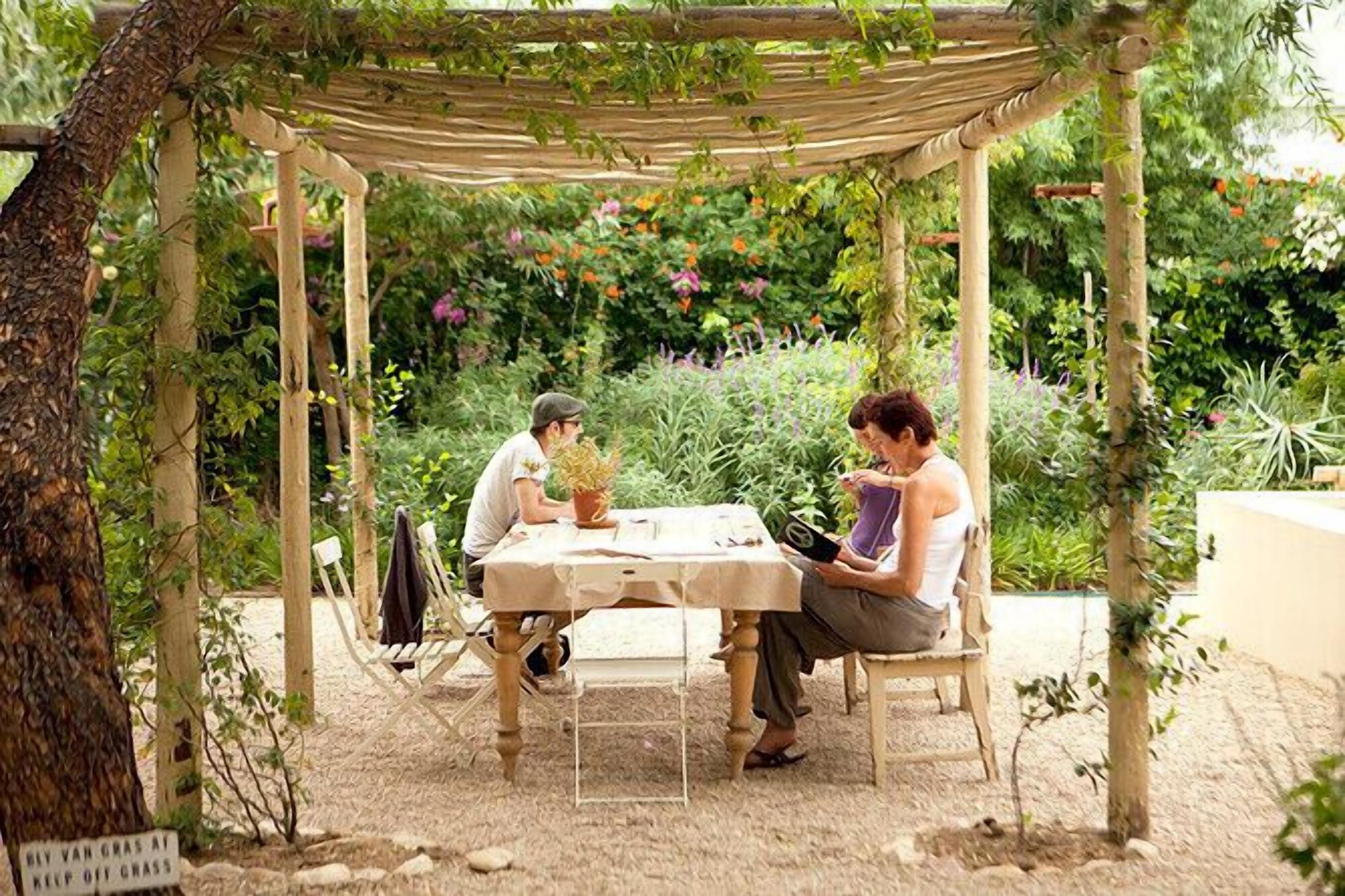 A wooden pergola with a table and chairs in a garden setting.