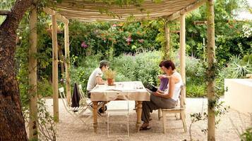 A wooden pergola with a table and chairs in a garden setting.