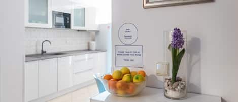 Una cucina moderna con mobili bianchi, una ciotola di frutta sul bancone e un quadro appeso al muro.