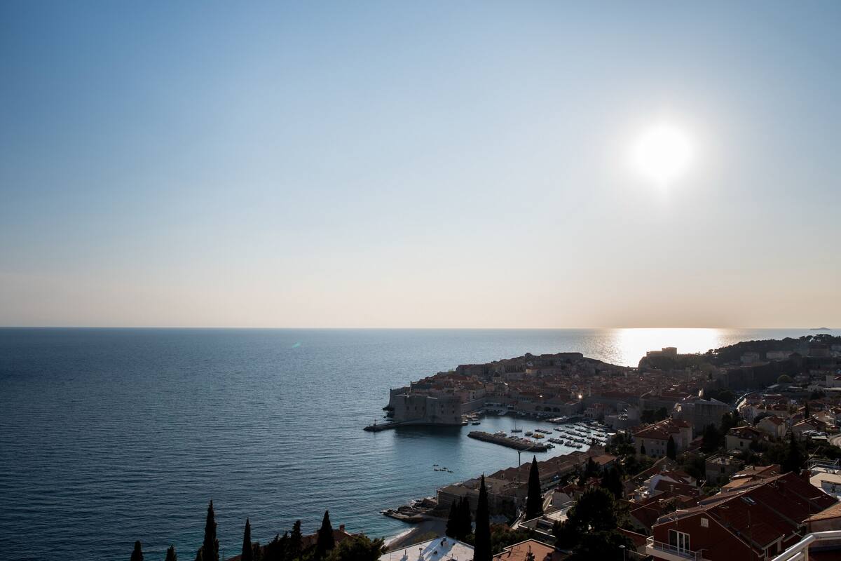 A coastal cityscape with a prominent historic fortification by the sea, clear skies, and a calm sea.
