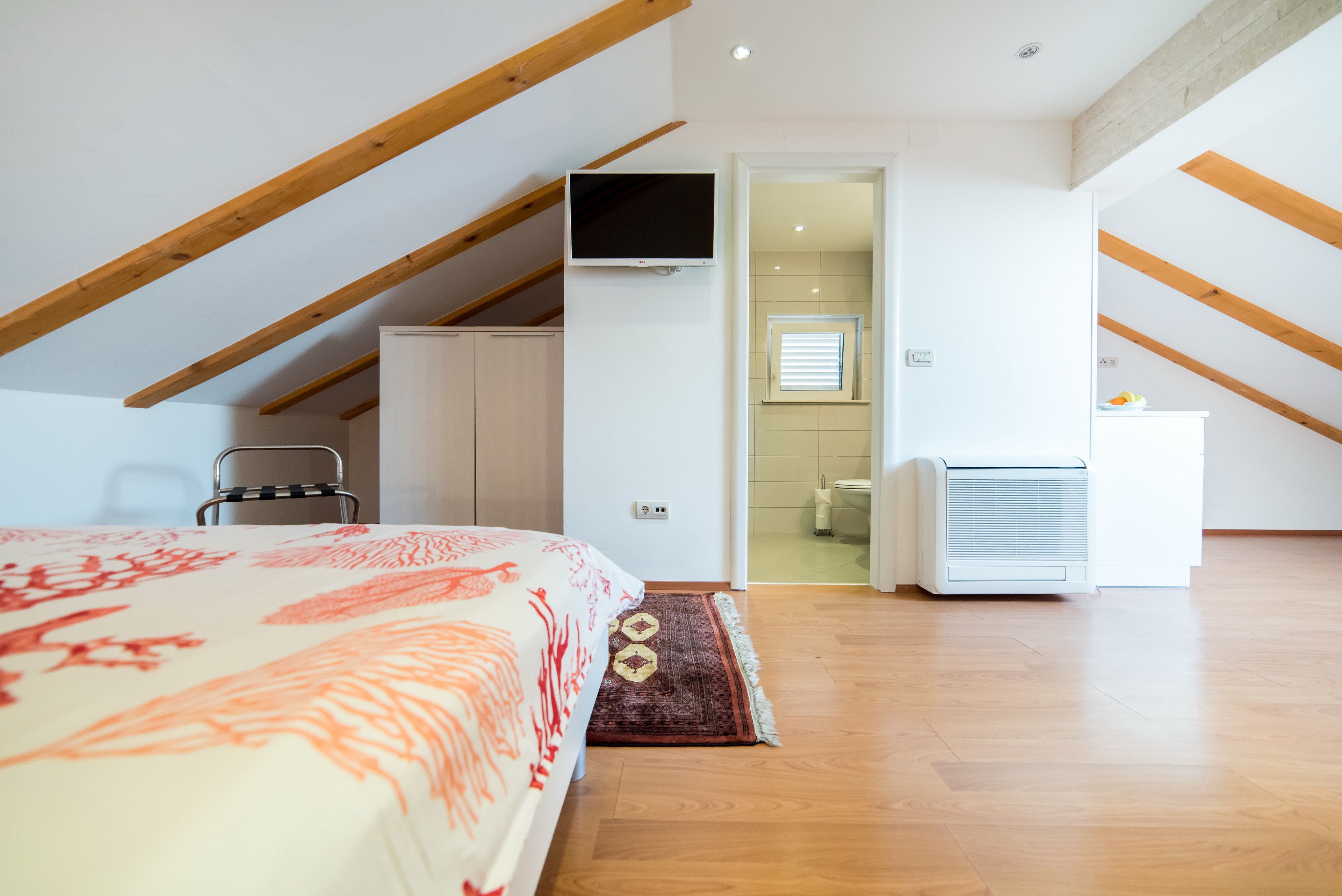 Un dormitorio con cama, televisión, escritorio y un baño visible a través de una puerta abierta.