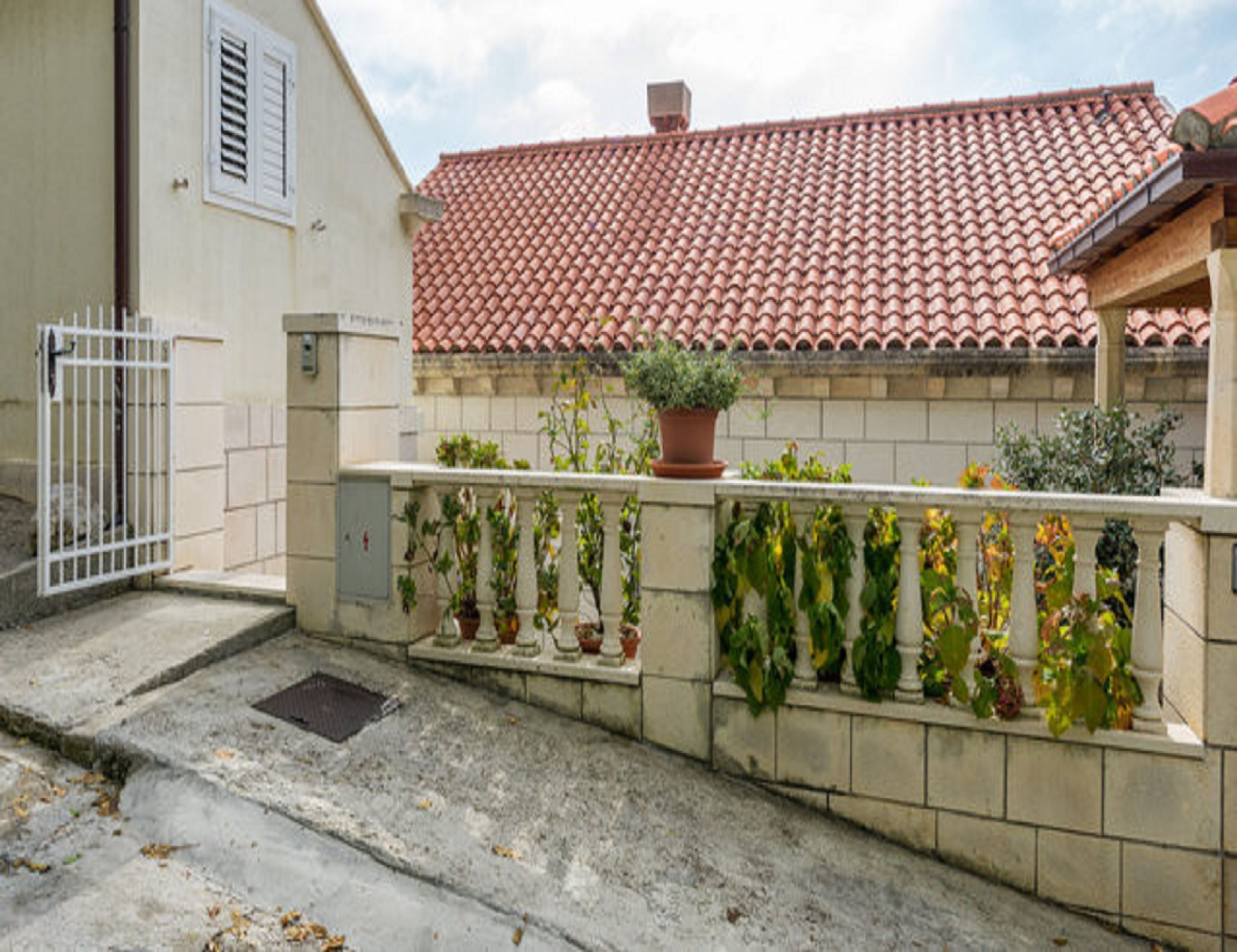 A building with a tiled roof, a gated entrance, and a balcony with potted plants.